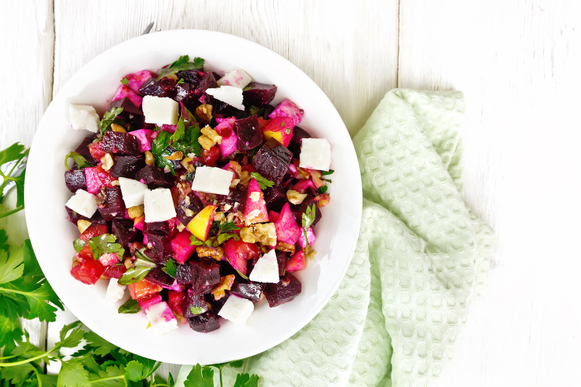 Salad with beetroot, feta cheese, apple, walnuts, parsley, seasoned with balsamic vinegar and olive oil in a plate, napkin against the background of a light wooden board on top